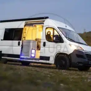 Citroën Jumper L3H2 Campervan mit offener Schiebetür, Blick ins beleuchtete Wohnmobil-Innere, Abendstimmung auf freiem Feld.