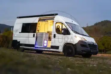 Citroën Jumper L3H2 Campervan mit offener Schiebetür, Blick ins beleuchtete Wohnmobil-Innere, Abendstimmung auf freiem Feld.