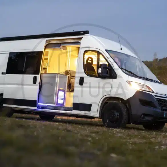 Citroën Jumper L3H2 Campervan mit offener Schiebetür, Blick ins beleuchtete Wohnmobil-Innere, Abendstimmung auf freiem Feld.