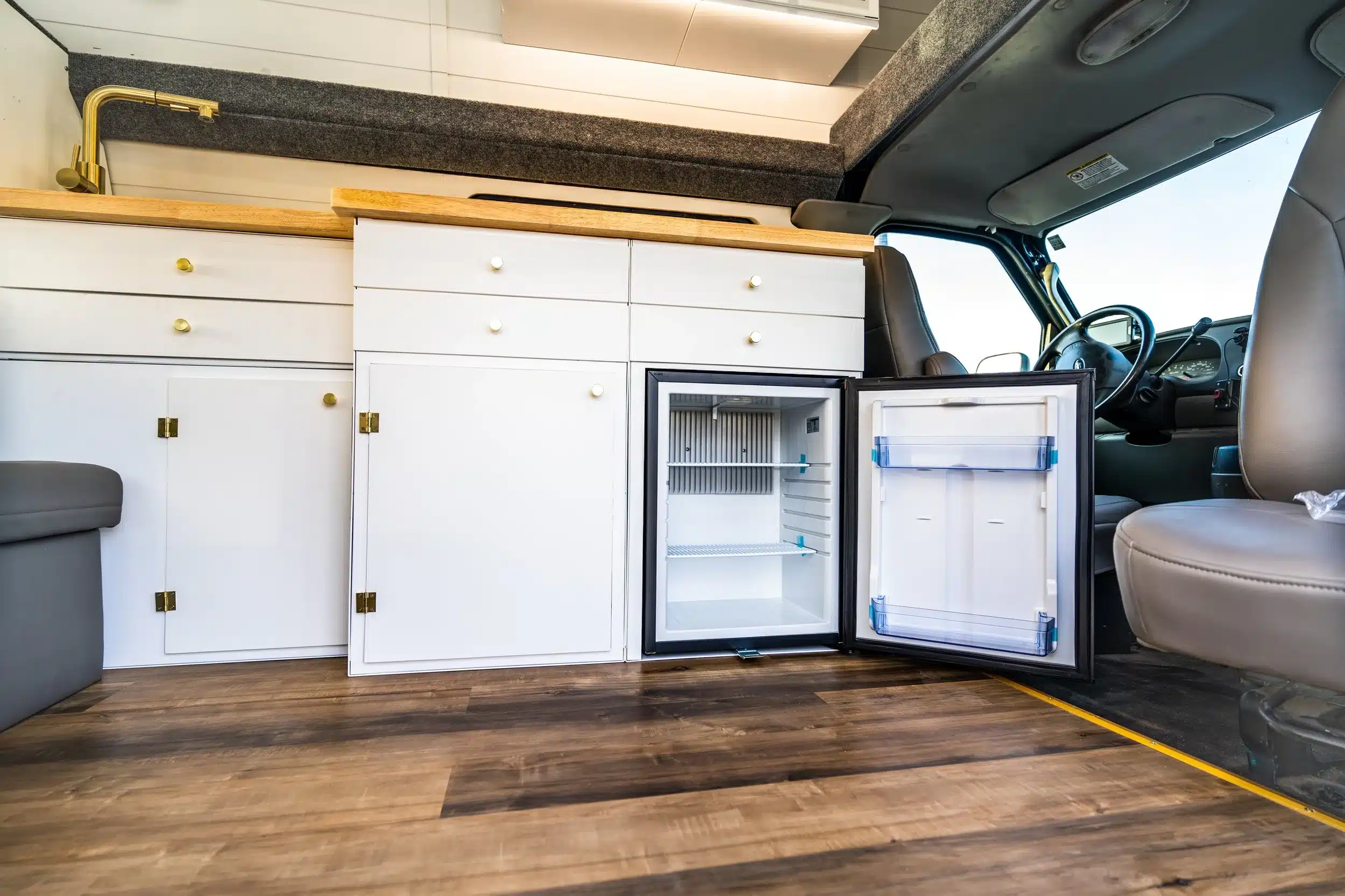 Helle Camper-Küchenzeile mit offenem Kühlschrank, goldenen Armaturen und Holzarbeitsplatte im Cobalt Cruiser