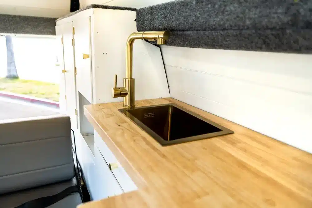 Campervan-Küchenzeile mit goldener Armatur und eingelassenem Spülbecken im modernen, hellen Innenraum des Cobalt Cruiser