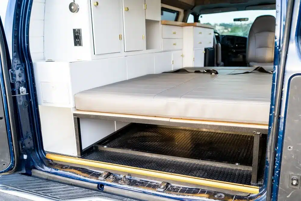 Innenansicht des Cobalt Cruiser Campervans mit herausgezogenem Bett, weißen Aluminiummöbeln und Stauraum.