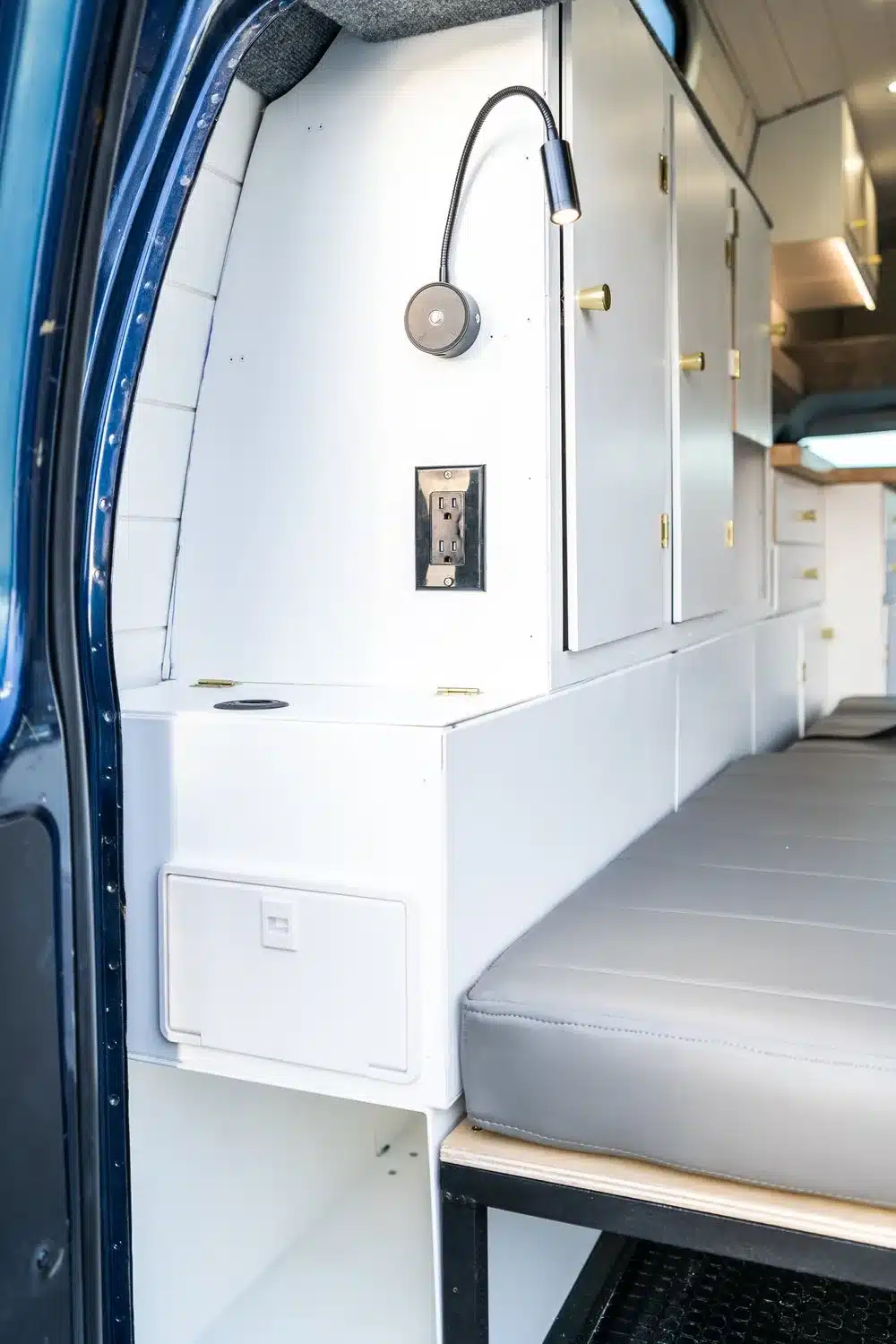 Weißer Innenraum eines Cobalt Cruiser Campervans mit goldenen Griffen, Leselampe und Steckdose.