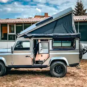 Land Rover Defender 110 Station Wagon mit geöffnetem Hubdach und Campingausbau, seitliche Ansicht im Freien