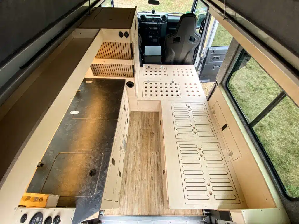 Innenausbau eines Land Rover Defender 110 mit L-förmigem Layout, Sitzbänken, Schränken und Klappbett.