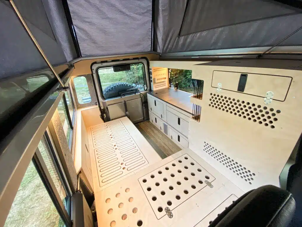 Blick in den ausgebauten Innenraum eines Land Rover Defender 110 mit Campingmöbeln und geöffnetem Hubdach