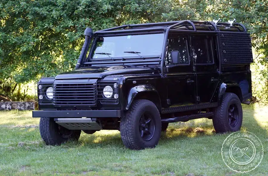 Land Rover Defender 110 SW TD4 mit Überrollkäfig, Offroad-Bereifung und individueller Ausstattung, geparkt auf einer Wiese