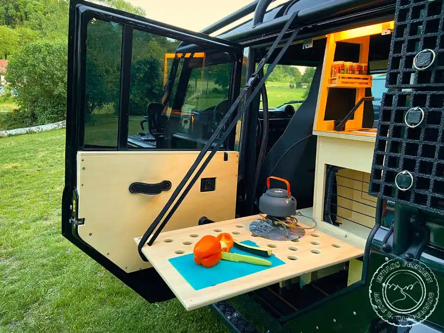 Outdoor-Küchentisch mit Schneidebrett und Wasserkocher am Land Rover Defender 110 SW Camper-Ausbau.