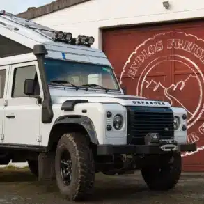 Land Rover Defender 110 SW TD4 2.2 mit Hubdach, Offroad-Bereifung, Seilwinde und Schnorchel vor einer Werkstatt