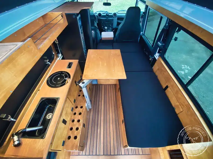 Ausgebauter Innenraum eines Land Rover Defender 110 mit Küchenmodul, Sitzbank und Campingtisch.