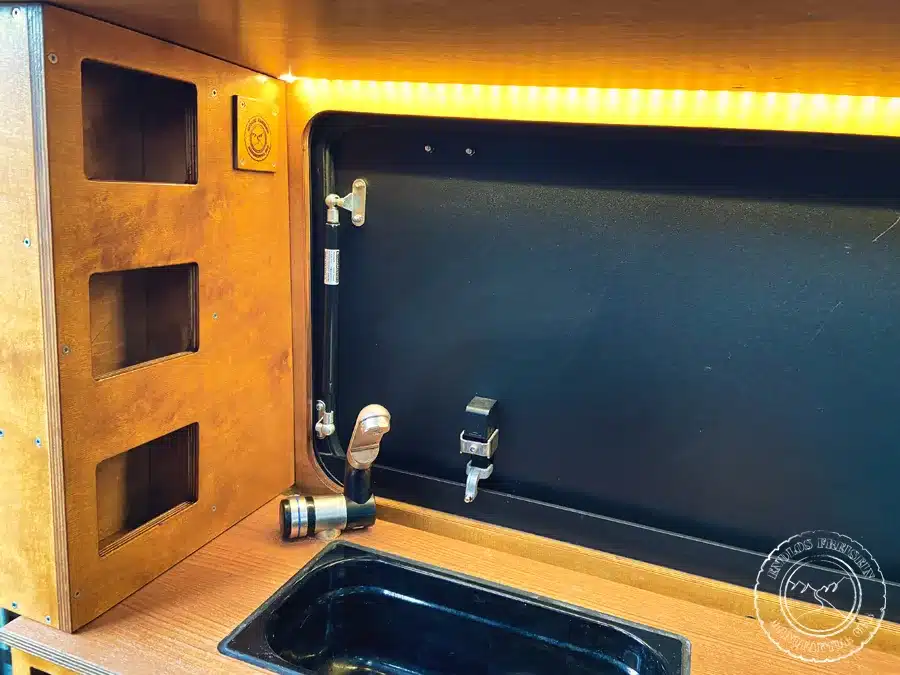 Innenausbau mit Spülbecken, Wasserhahn, LED-Leiste und offenem Holzregal im Defender 110 Camper.