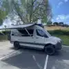 Adventure-Van „The Bear“ auf Mercedes Sprinter 144-Chassis mit ausgefahrener Markise auf Parkplatz