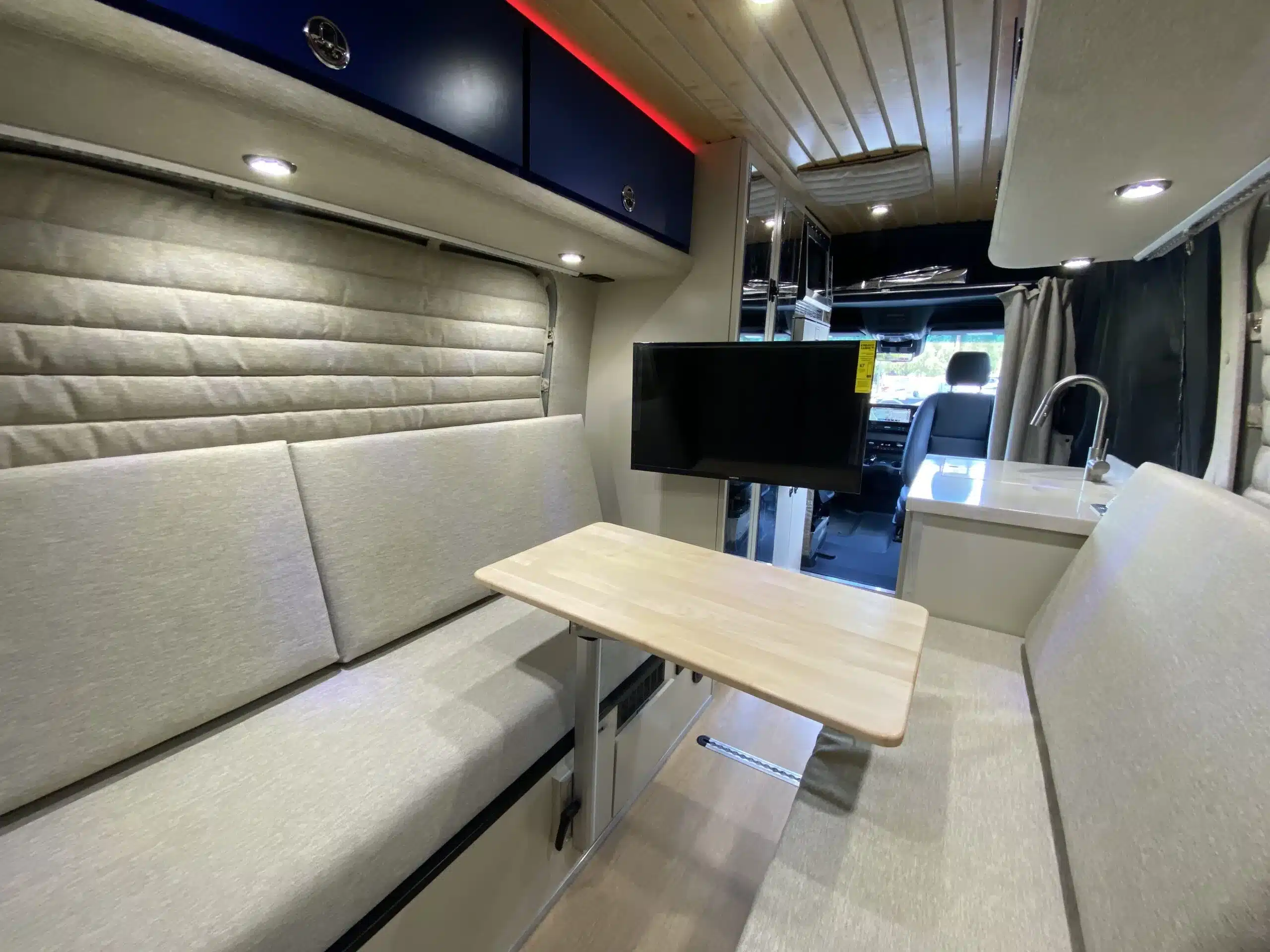 Gemütlicher Wohnbereich und Küche im Mercedes Sprinter Campervan „The Bear“ mit Dinette, TV und modernem Ausbau.