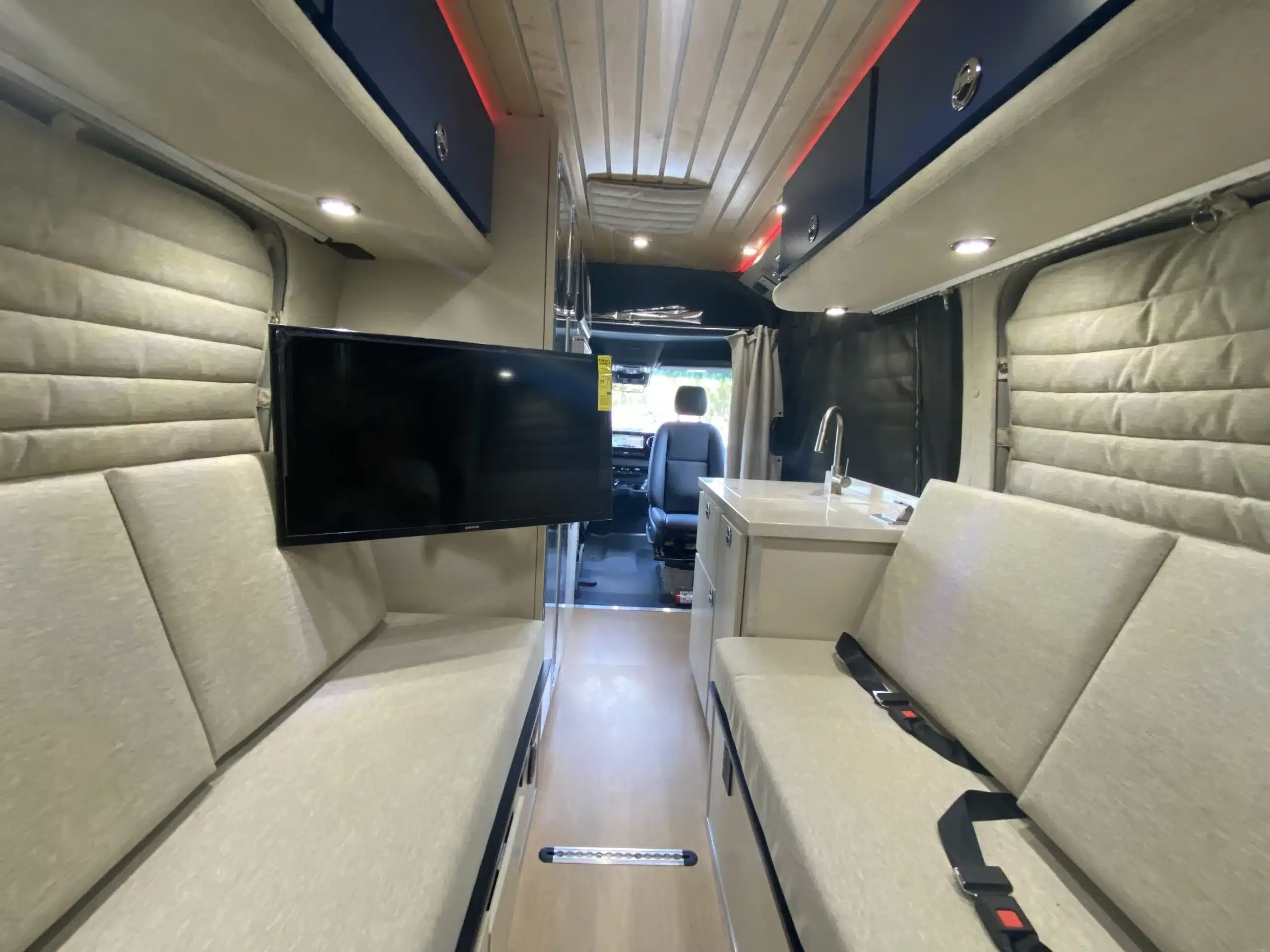 Innenansicht eines umgebauten Mercedes Sprinter-Vans 'The Bear' mit Sofa, Küchenzeile und Fernseher.