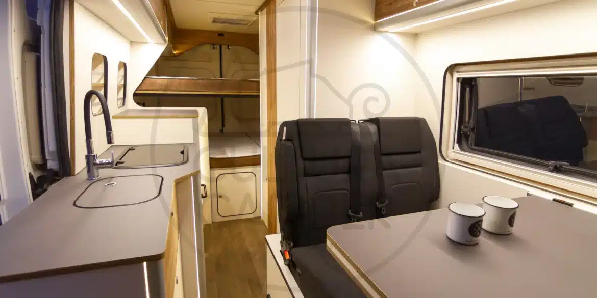 Innenraum eines Ducato L4H2 Campervans mit Küchenzeile, Sitzgruppe und Etagenbett, geeignet für Familienreisen und Vanlife mit Hunden.