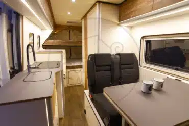 Innenraum eines Ducato L4H2 Campervans mit Küchenzeile, Sitzgruppe und Etagenbett, geeignet für Familienreisen und Vanlife mit Hunden.