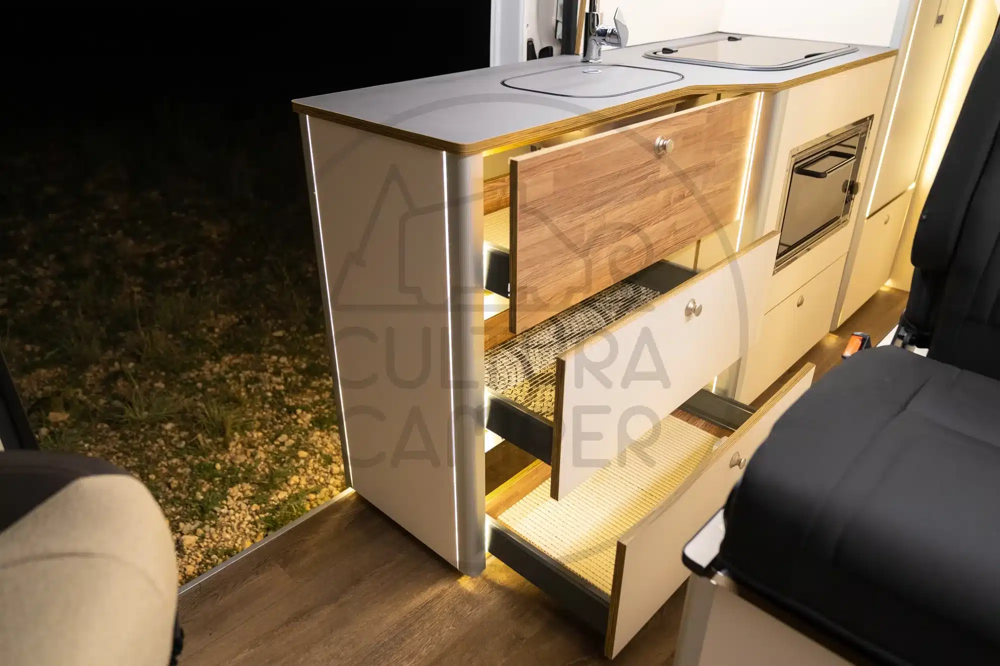 Küchenblock im Ducato-Camper mit offener Schubladenbeleuchtung und Kochfeld bei Nachtaufnahme.