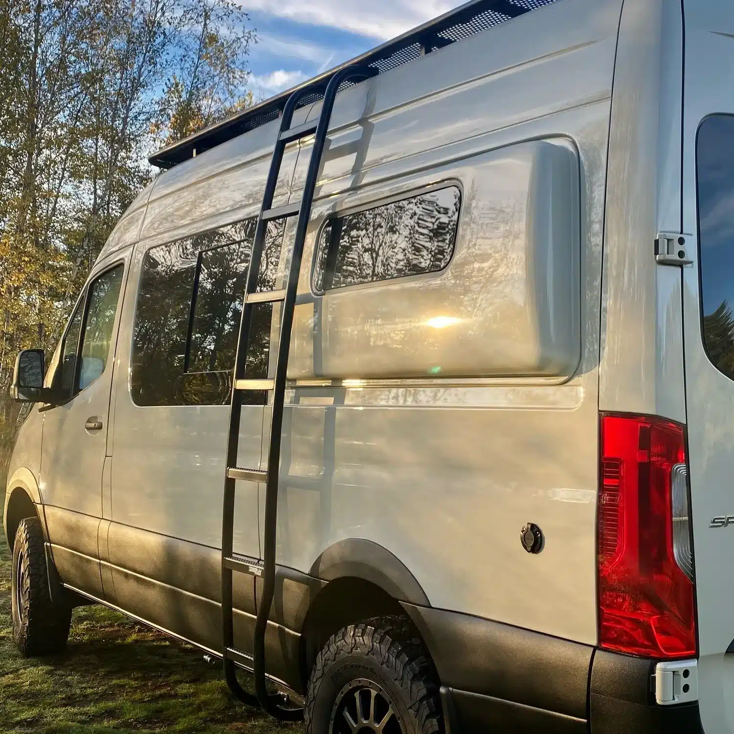 TanVan Campervan auf Mercedes-Sprinter-Basis mit Leiter und Offroad-Reifen bei Sonnenuntergang