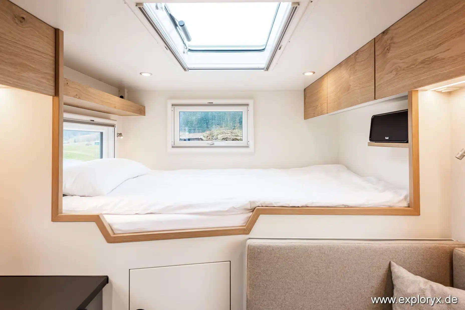 Blick auf das quer eingebaute Doppelbett mit Stauraum und Dachfenster im Expeditionsmobil Exploryx Impala Daily XL.