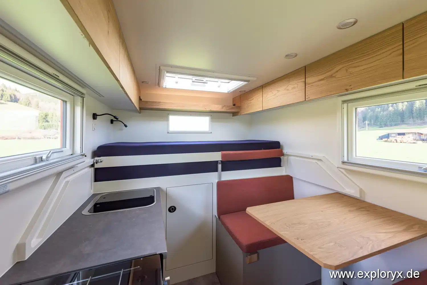 Innenraum des Exploryx Impala Daily XXXV mit Sitzgruppe, Bett, Fenstern und Küchenzeile.