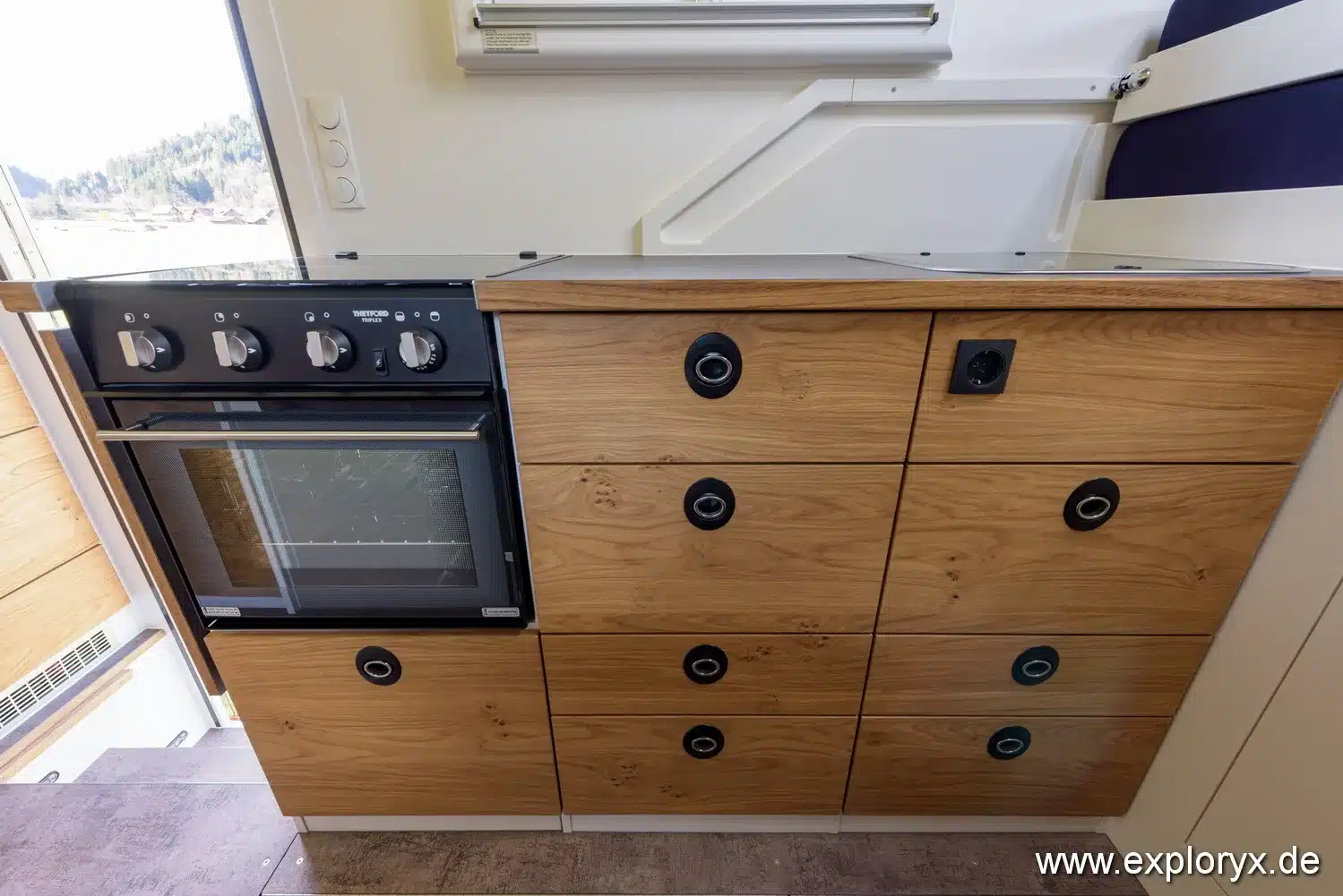 Moderne Küchenzeile mit Holzfronten und Backofen im Innenraum des Exploryx Impala Daily XXXV Reisemobils.