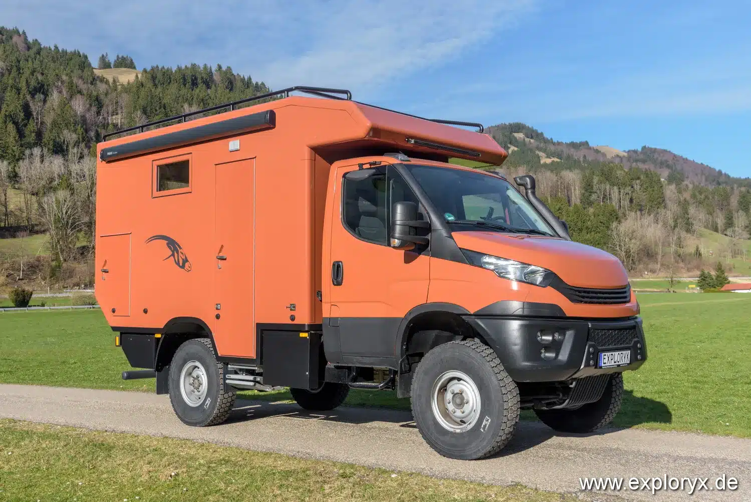 Exploryx Impala Daily XXXV: Offroad-Reisemobil auf Iveco Daily 4x4 Fahrgestell für autarkes Reisen abseits befestigter Straßen, orange lackiert, mit Dachreling und Alkoven.