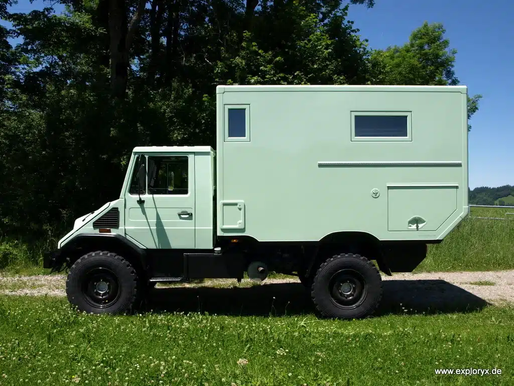 Seitenansicht eines mintgrünen Exploryx Klippspringer U140L Expeditionsmobils auf Mercedes-Benz Unimog-Basis vor grünem Hintergrund.