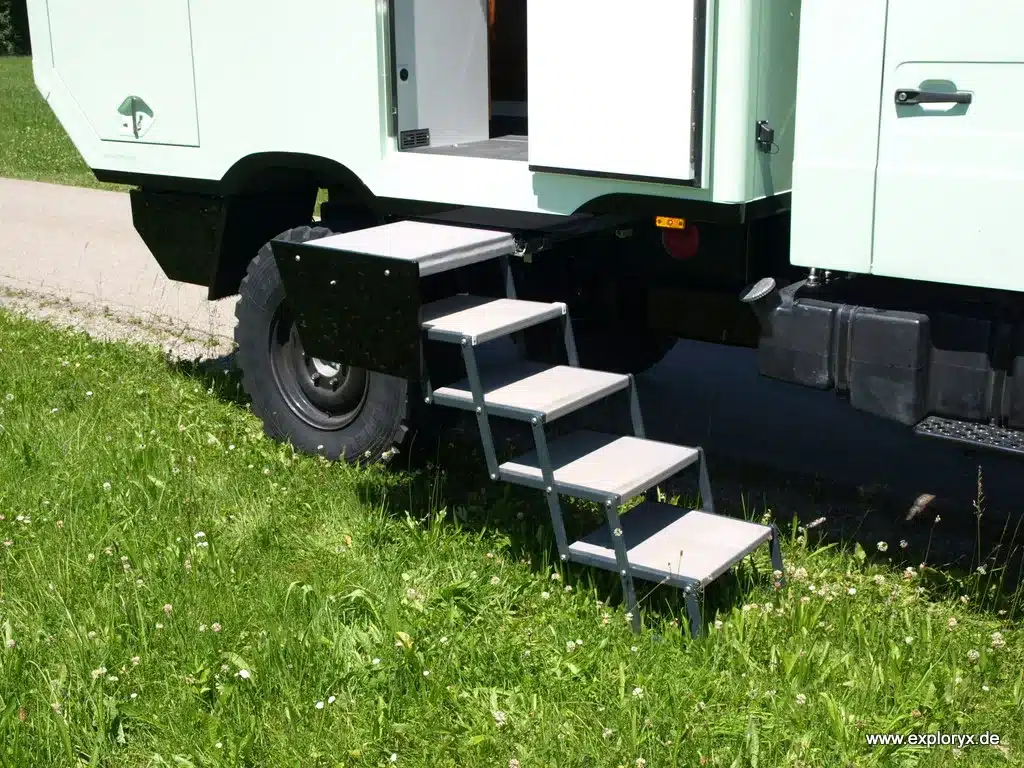Einstiegstreppe an einem mintgrünen Exploryx Klippspringer U140L Expeditionsmobil, geparkt auf einer Wiese.