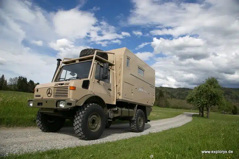 Expeditionsfahrzeug Exploryx Klippspringer U1550 L basierend auf Mercedes Unimog steht auf einem Feldweg bei bewölktem Himmel