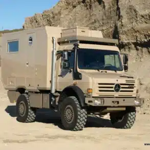 Exploryx Klippspringer U4000 Expeditionsmobil auf Unimog-Basis in beigefarbener Lackierung, seitliche Ansicht in einer sandigen Umgebung.