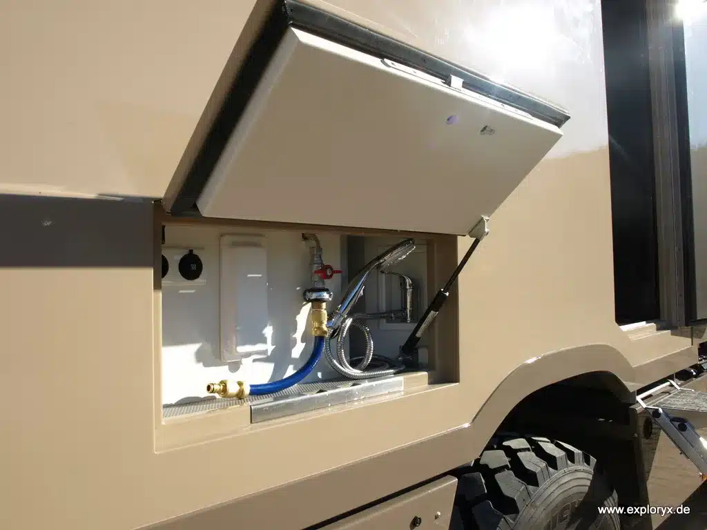 Außenwasseranschluss des Exploryx Klippspringer U4000 mit Schlauch und Wasserhahn, eingebaut in die Seitenwand des Fahrzeugs.
