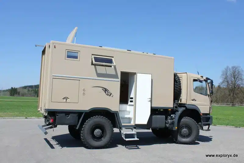 Exploryx Nyala Axor Expeditionsmobil auf Basis des Mercedes-Benz Axor 4x4, seitliche Ansicht mit geöffneter Tür, auf freiem Gelände.