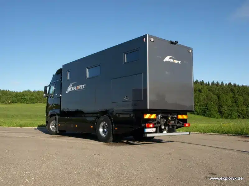 Seitliche und hintere Ansicht des Exploryx Nyala FH16 Expeditions-Trucks auf Basis eines Volvo FH16, abgestellt auf Asphalt vor grüner Landschaft