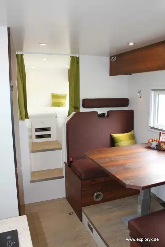 Blick auf die Sitzgruppe mit Tisch und den offenen Schlafbereich im Exploryx Nyala FH16 Expeditionsmobil