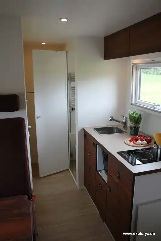 Moderne Küche und Wohnraum im Expeditionsfahrzeug Exploryx Nyala FH16 mit Induktionskochfeld, Spüle und Holzdekoren.