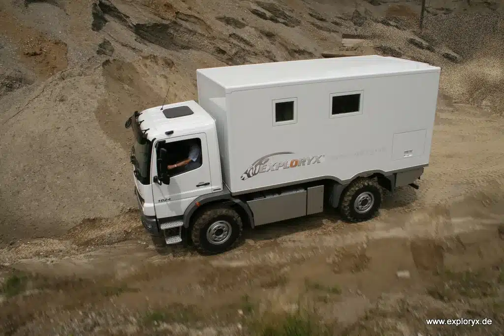 Expeditionsmobil Exploryx Nyala I auf Mercedes Atego 1024 4x4 fährt durch sandiges Gelände.