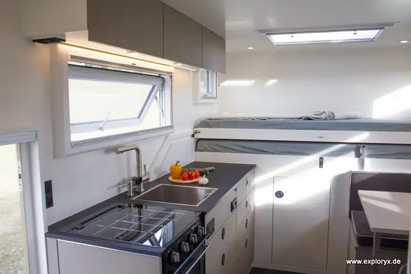 Innenraum des Exploryx Nyala MAN mit Küchenzeile, Herd, Spüle, Sitzgruppe und ausziehbarem Einzelbett.