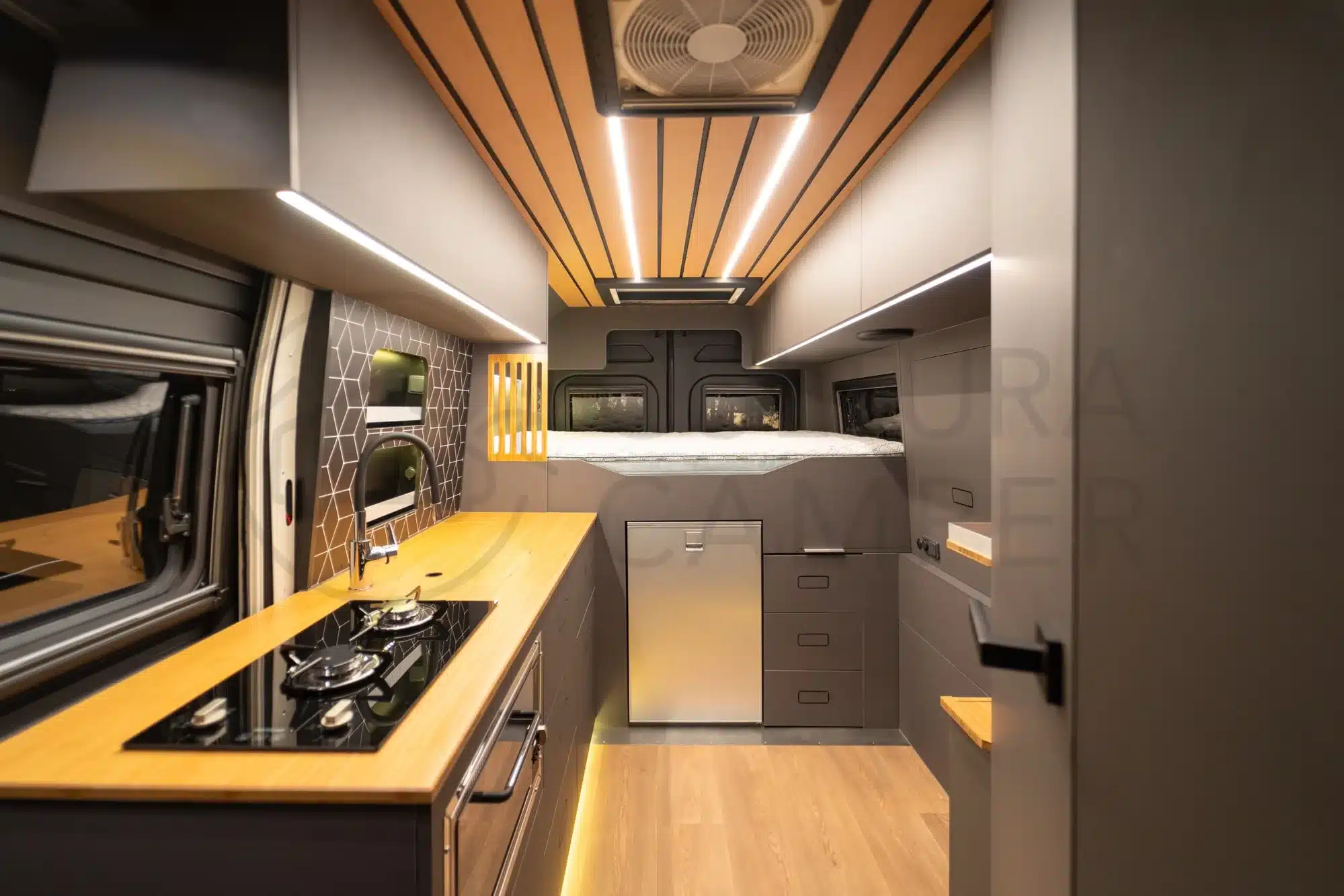 Innenraum eines Fiat Ducato Oficina Móvil mit Küche, Bett und viel Stauraum, ausgeleuchtet mit LED-Beleuchtung.