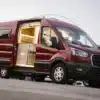 Ford Transit L2H2 Campervan mit offenem Einstieg und individuellem Innenausbau auf einem Parkplatz.