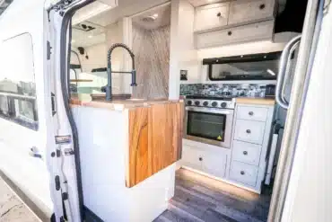 Innenansicht einer hochwertigen Camper-Küche im Ford Transit 350 mit Holzarbeitsplatte, Gasherd und Schränken.