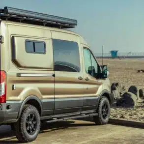 Ford Transit Campervan mit Allradantrieb, Dachträger und ausgebautem Innenraum, geparkt am Sandstrand.
