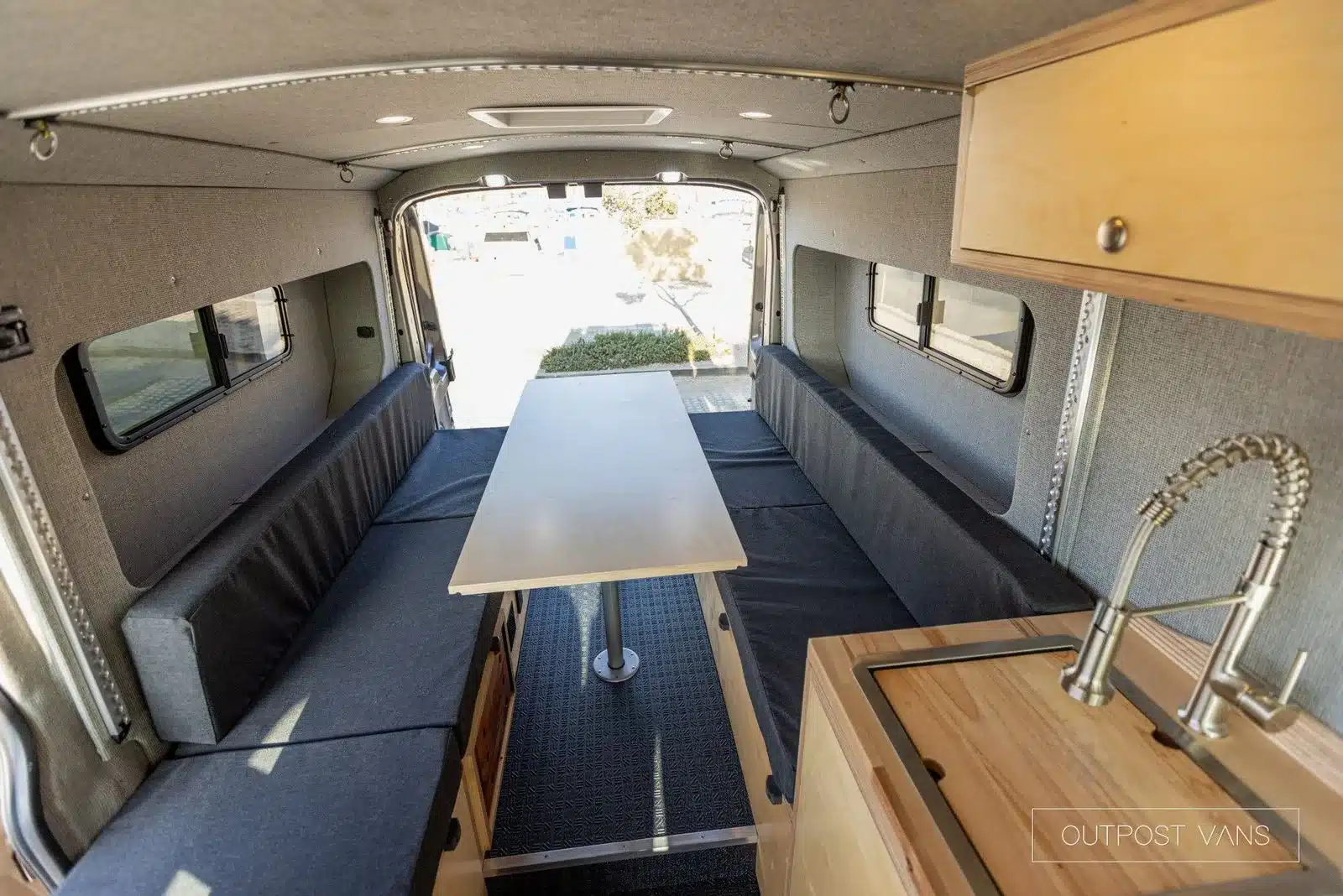 Innenraum eines ausgebauten Ford Transit Campervans mit Sitzbänken, Tisch und Küchenzeile