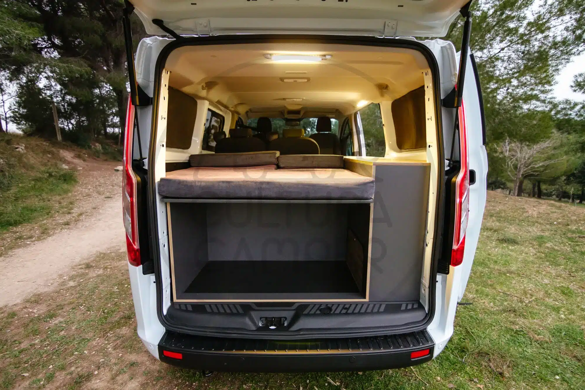 Heckansicht eines Ford Transit Custom Campers mit offenem Kofferraum, Stauraum und Schlafbereich.