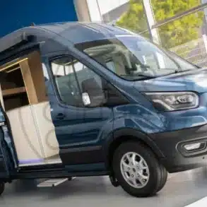 Ford Transit L3 H3 Camper mit geöffneter Schiebetür und sichtbarem Innenausbau im Ausstellungsraum.