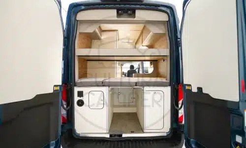 Innenansicht eines ausgebauten Ford Transit L3 H3 Campers mit Hochbett, Stauraum und Möbeln.