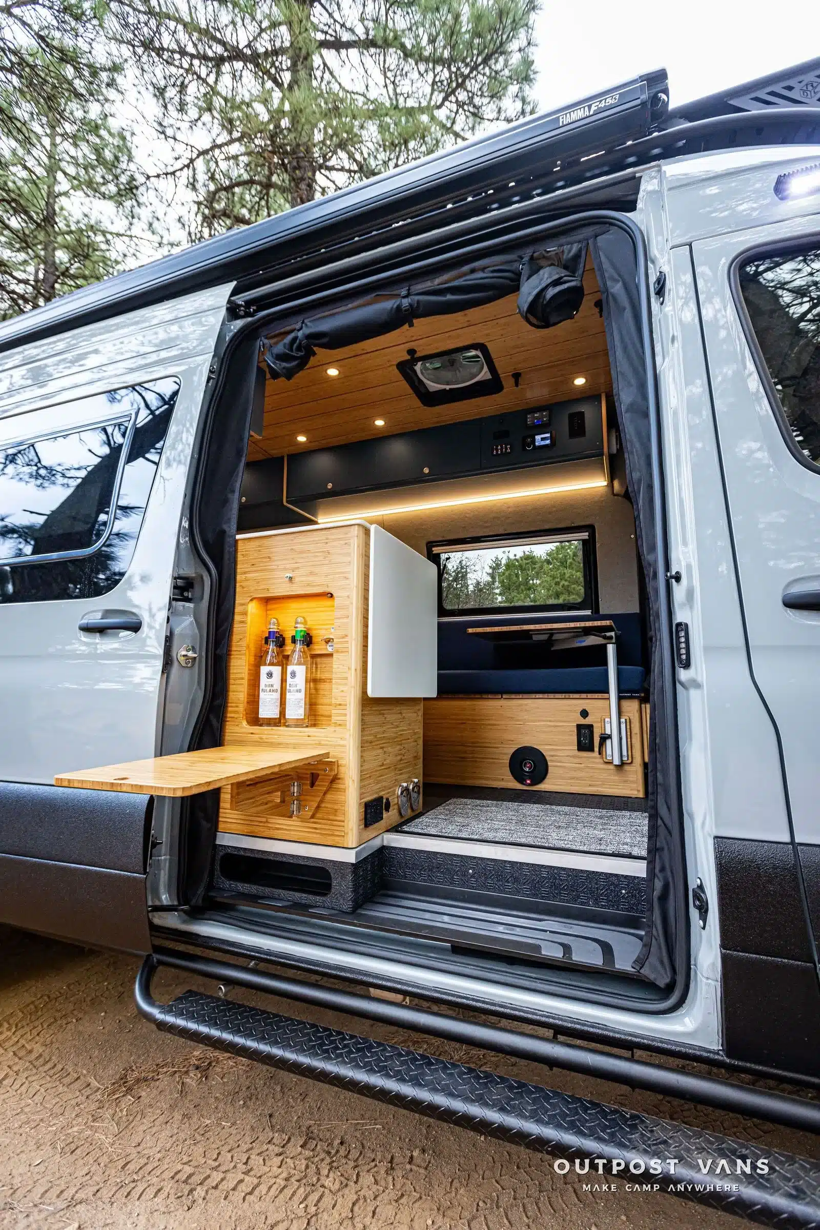 Außenansicht eines geöffneten Sprinter-Campingvans mit ausklappbarer Bambustheke und Blick in den modernen Innenraum.