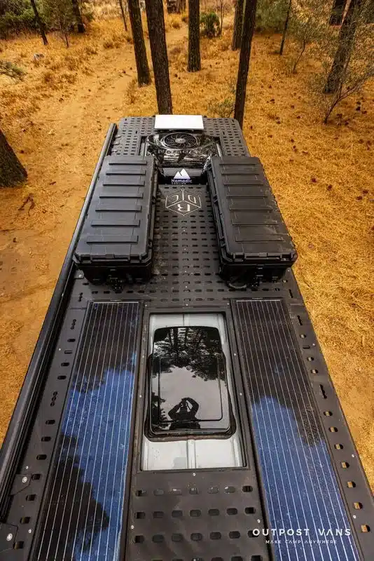 Blick von oben auf das Dach eines Offroad-Campingfahrzeugs mit Solarmodulen, Staukästen und Dachträger im Wald