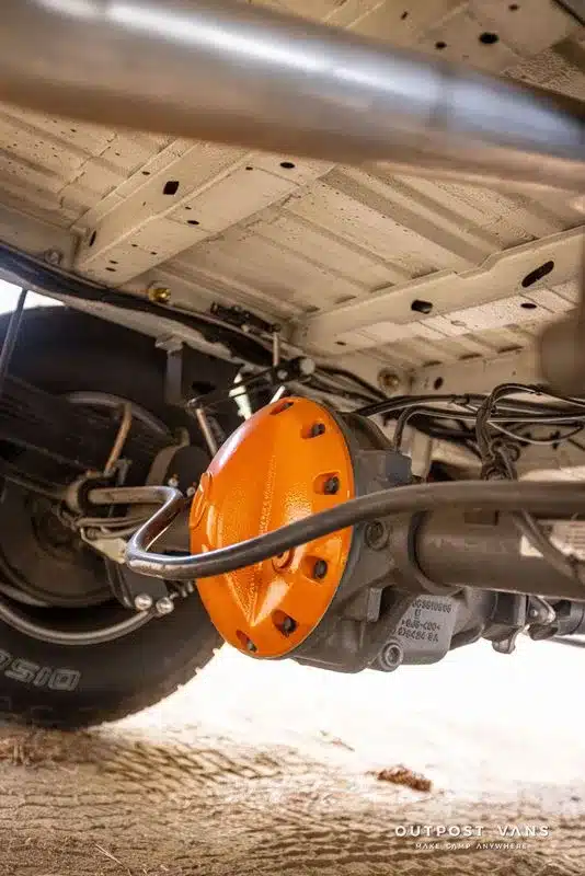Leuchtend orangefarbener Differenzialdeckel am robusten Unterboden des Güero-Campingausbaus auf Sprinter-Basis.