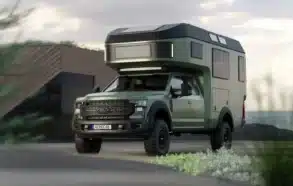 Expeditionsmobil Gehocab Edge Explorer Trail mit 4x4-Antrieb und aufgesetzter Wohnkabine, steht vor einem modernen Gebäude.