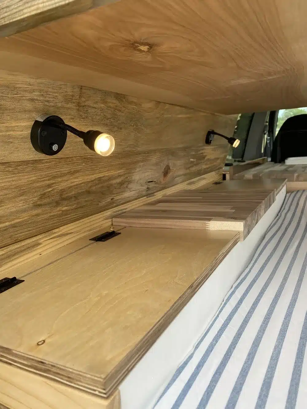 Innenansicht eines individuellen Camper-Ausbaus mit Holzverkleidung, Stauraumklappen und LED-Leseleuchten
